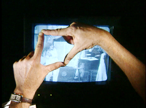 Les index et les pouces de deux mains se joignent devant un écran de télévision