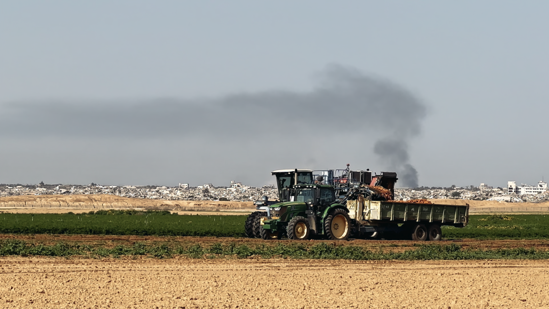Au premier plan, des terres agricoles et un tracteur. À l'arrière plan, un territoire désolé, détruit et sous les bombes.
