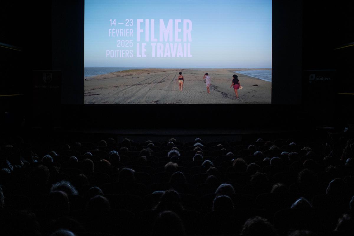 Photo d'une salle de cinéma. À l'écran, une image de plage avec écrit Filmer le travail © Malia Chaton